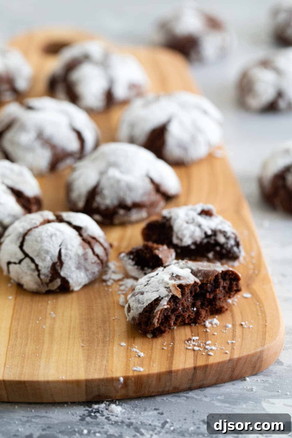A rustic wooden cutting board laden with an assortment of freshly baked chocolate crinkle cookies, ready to be enjoyed.