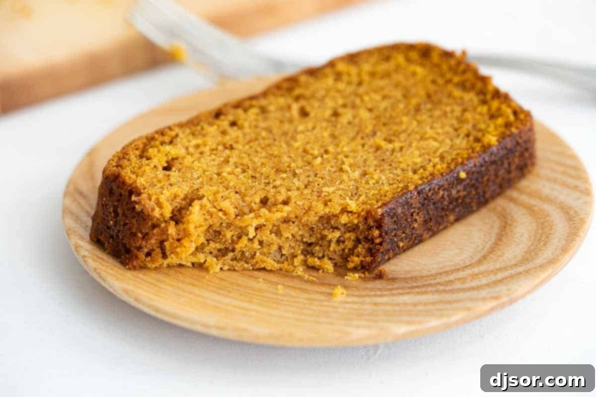 A single, thick slice of moist pumpkin bread elegantly placed on a white plate, highlighting its deliciousness.
