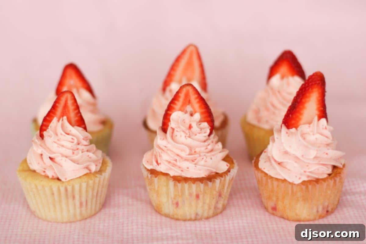 Six beautifully decorated strawberry cupcakes with fresh strawberry slices on top, arranged on a white plate.