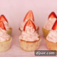 A close-up of six strawberry cupcakes, each topped with a swirl of pink strawberry meringue buttercream and a fresh strawberry slice.