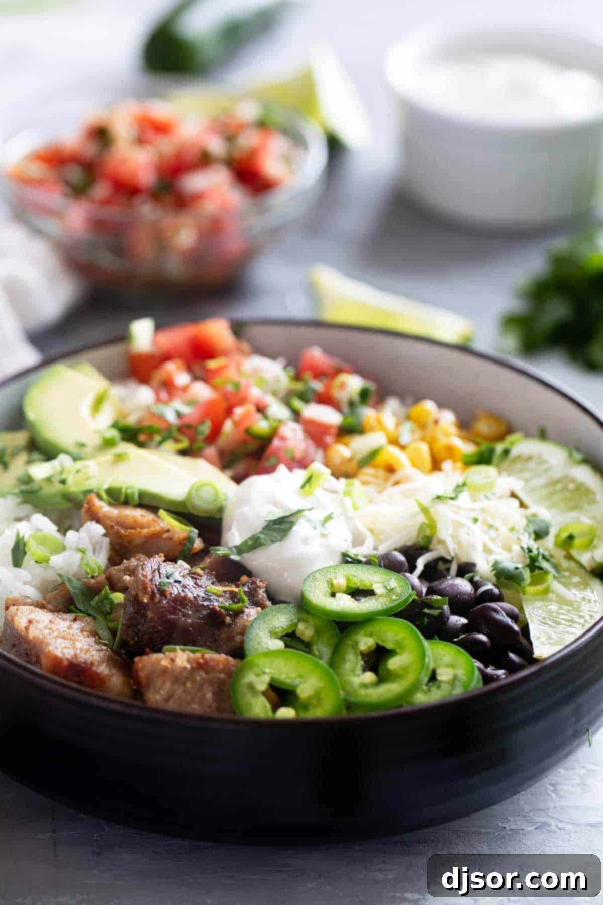 A close-up shot of a beautifully assembled Pork Carnitas Burrito Bowl, showcasing the golden-brown carnitas, fresh pico de gallo, melted cheese, and a swirl of sour cream, ready to be enjoyed.