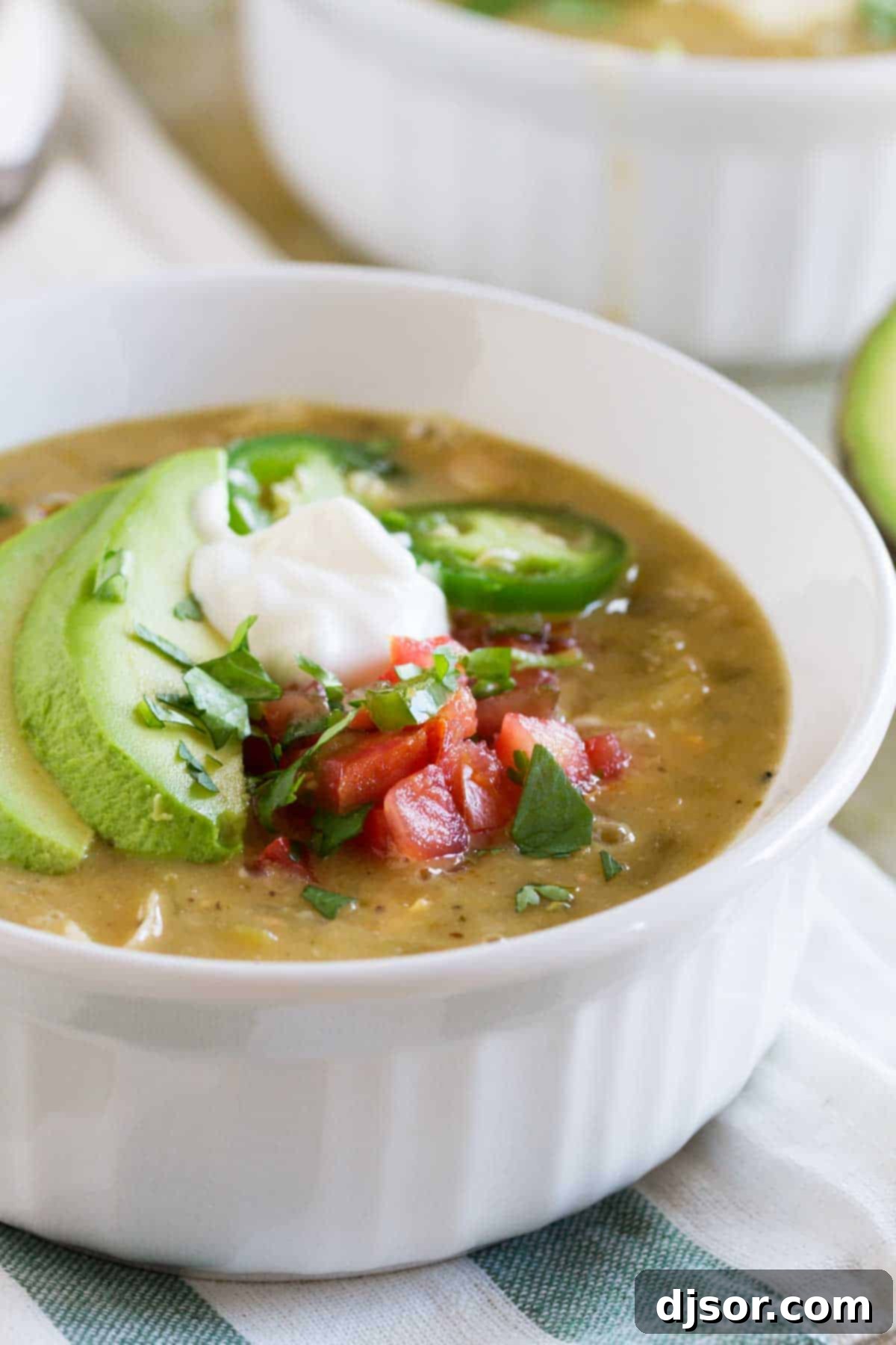 A close-up of vibrant toppings for White Chicken Chili, including fresh cilantro, sour cream, and shredded cheese.