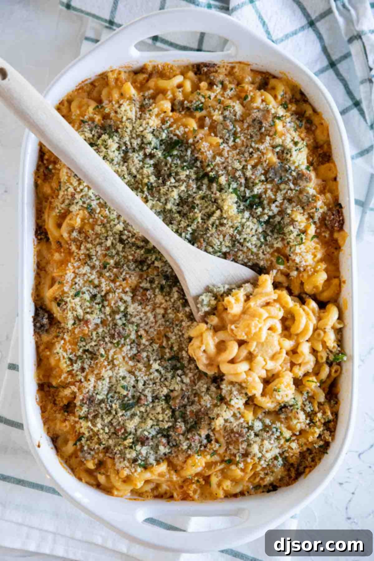 An overhead view of a casserole dish filled with bubbling Buffalo Chicken Mac and Cheese, with a wooden spoon ready to serve.