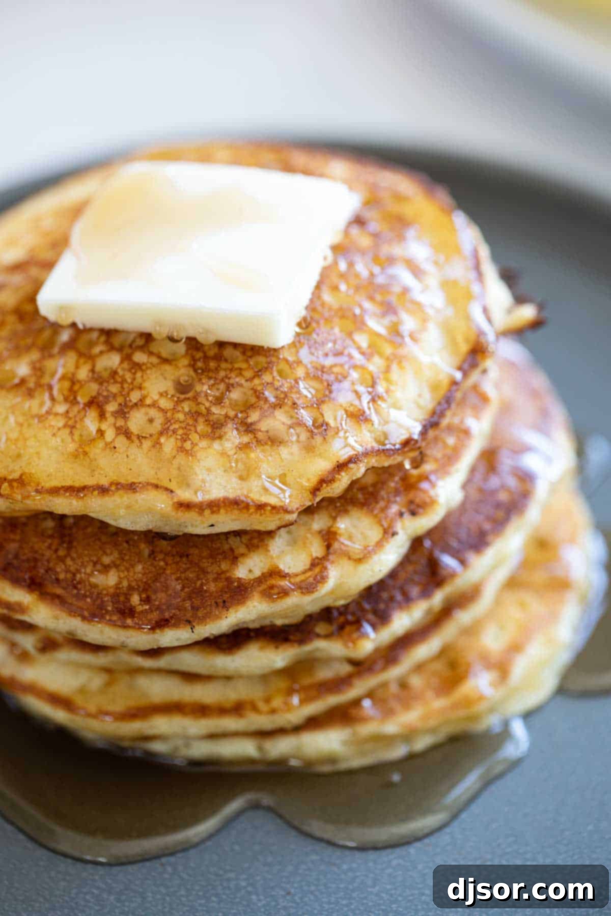 Cornmeal Pancakes with Classic Toppings A stack of golden Cornmeal Pancakes, generously topped with a square of melting butter and glistening with maple syrup.