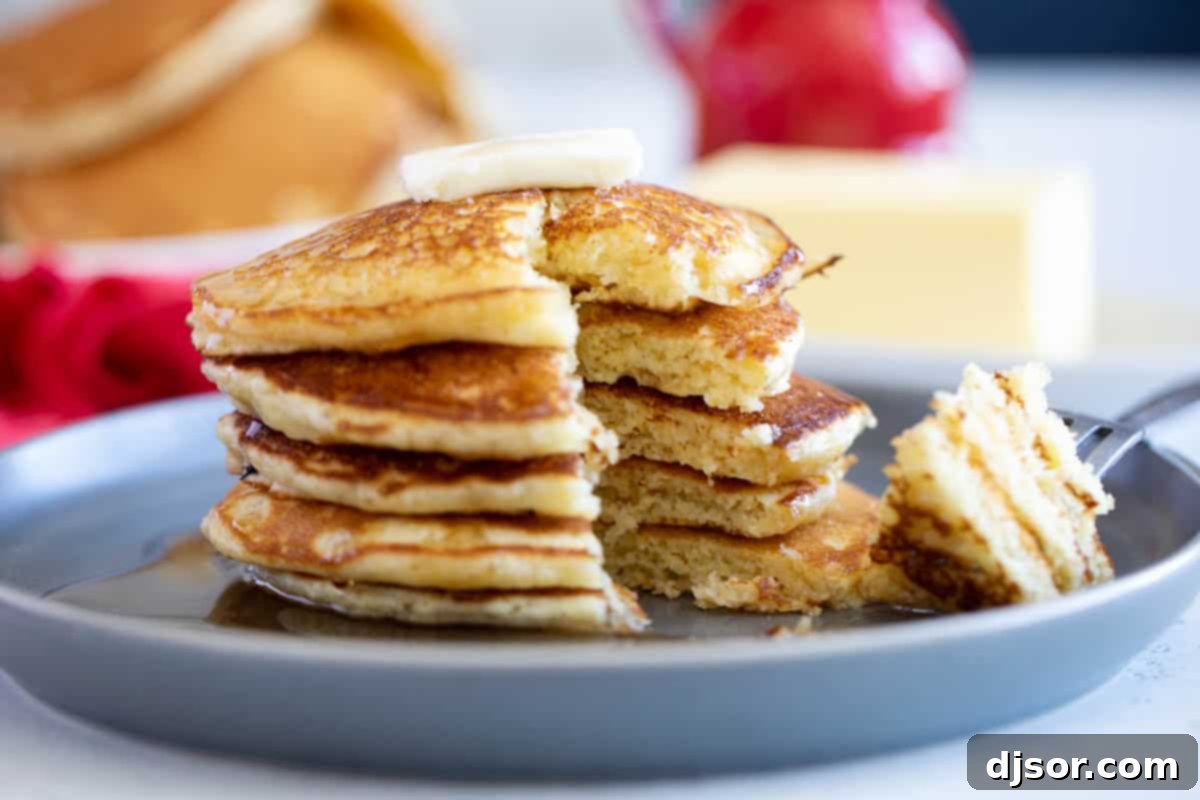 Enjoying a Bite of Cornmeal Pancake A close-up shot of a stack of cornmeal pancakes with a bite taken out of the top one, revealing its fluffy interior.