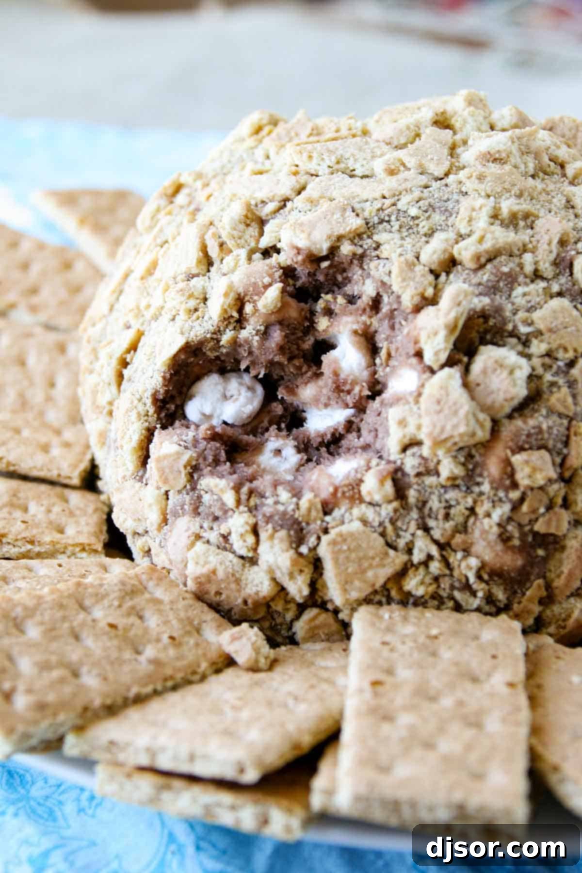 A S'mores cheese ball on a serving platter with a scoop taken out, revealing the marshmallow-filled center.