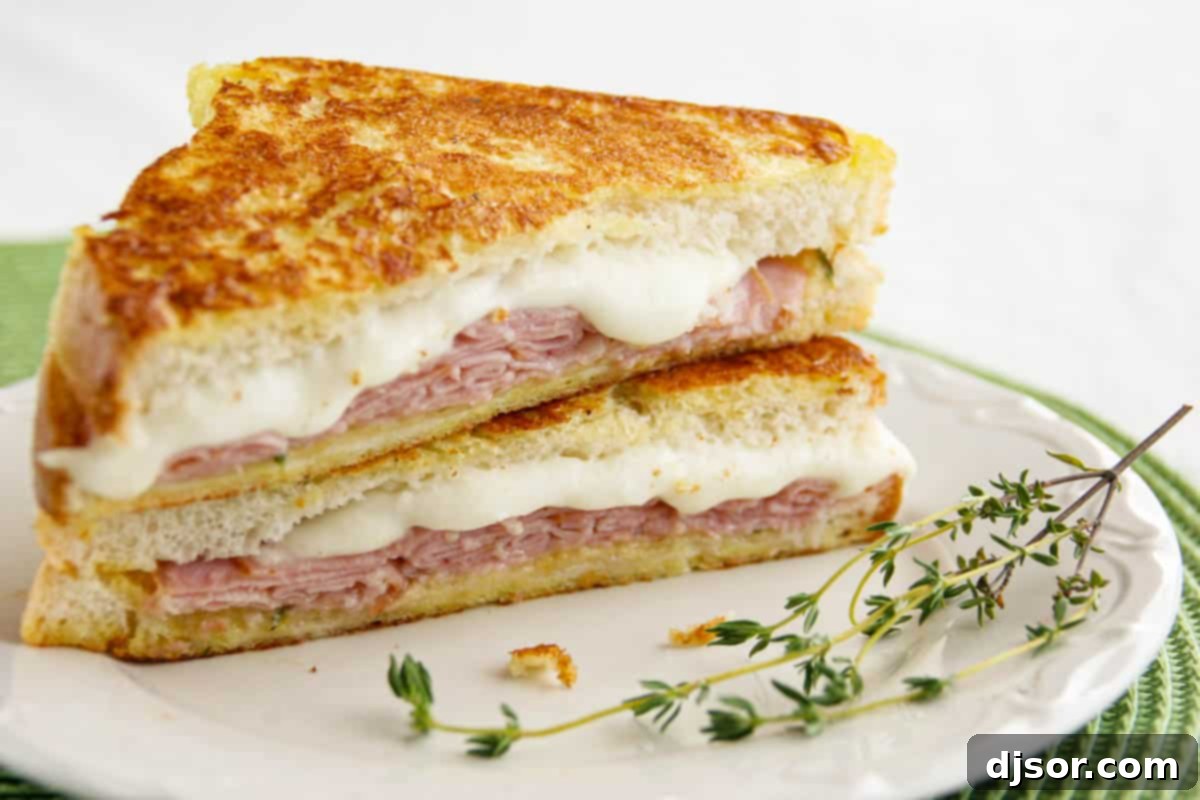 Tuscan Monte Cristos 2 Italian Style Monte Cristo cut in half and stacked with fresh thyme on a plate, showcasing melted mozzarella and ham.
