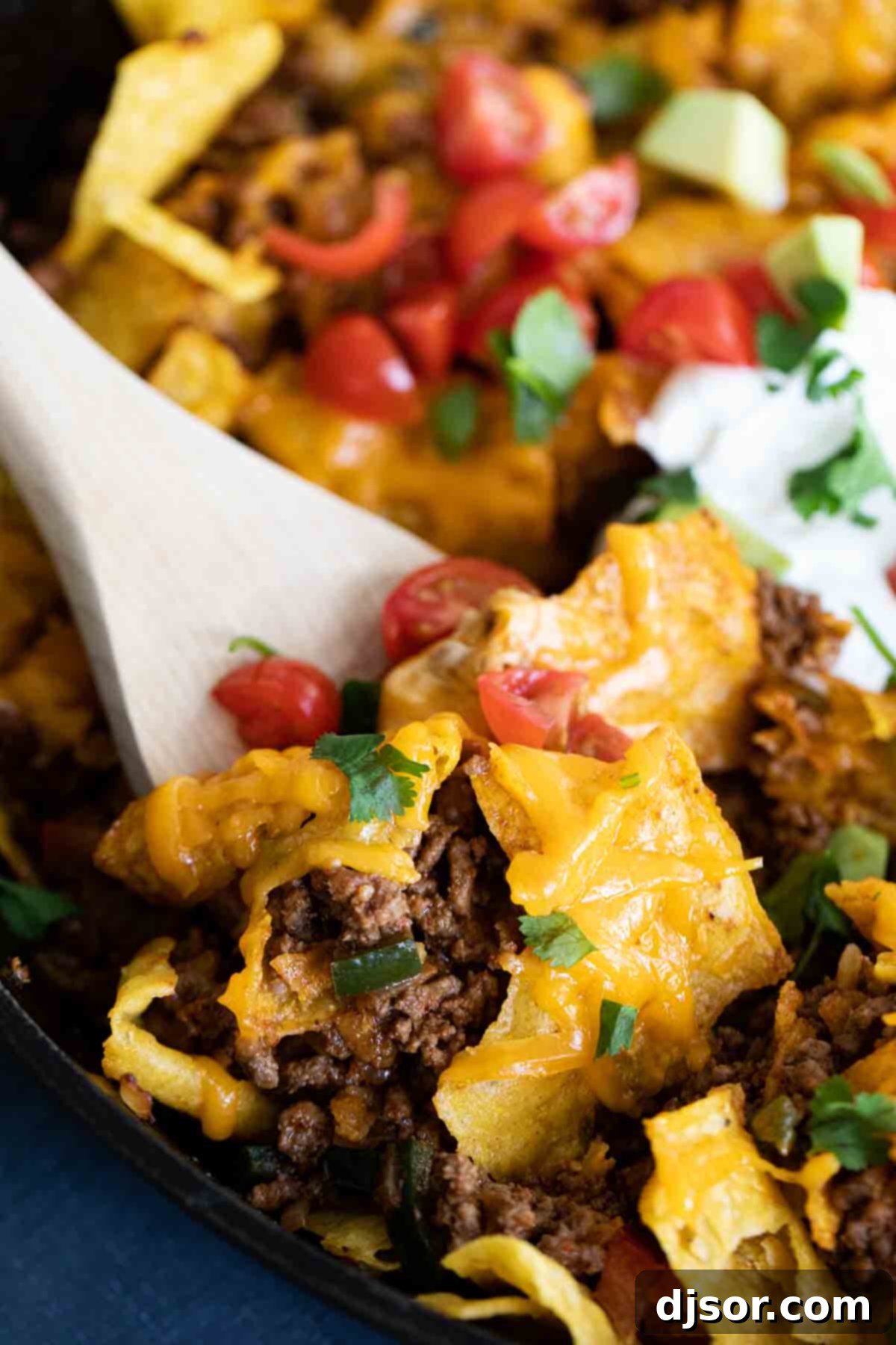A wooden spoon scooping out a portion of the cheesy, meaty Taco Skillet with tortilla chips from a cast iron pan.