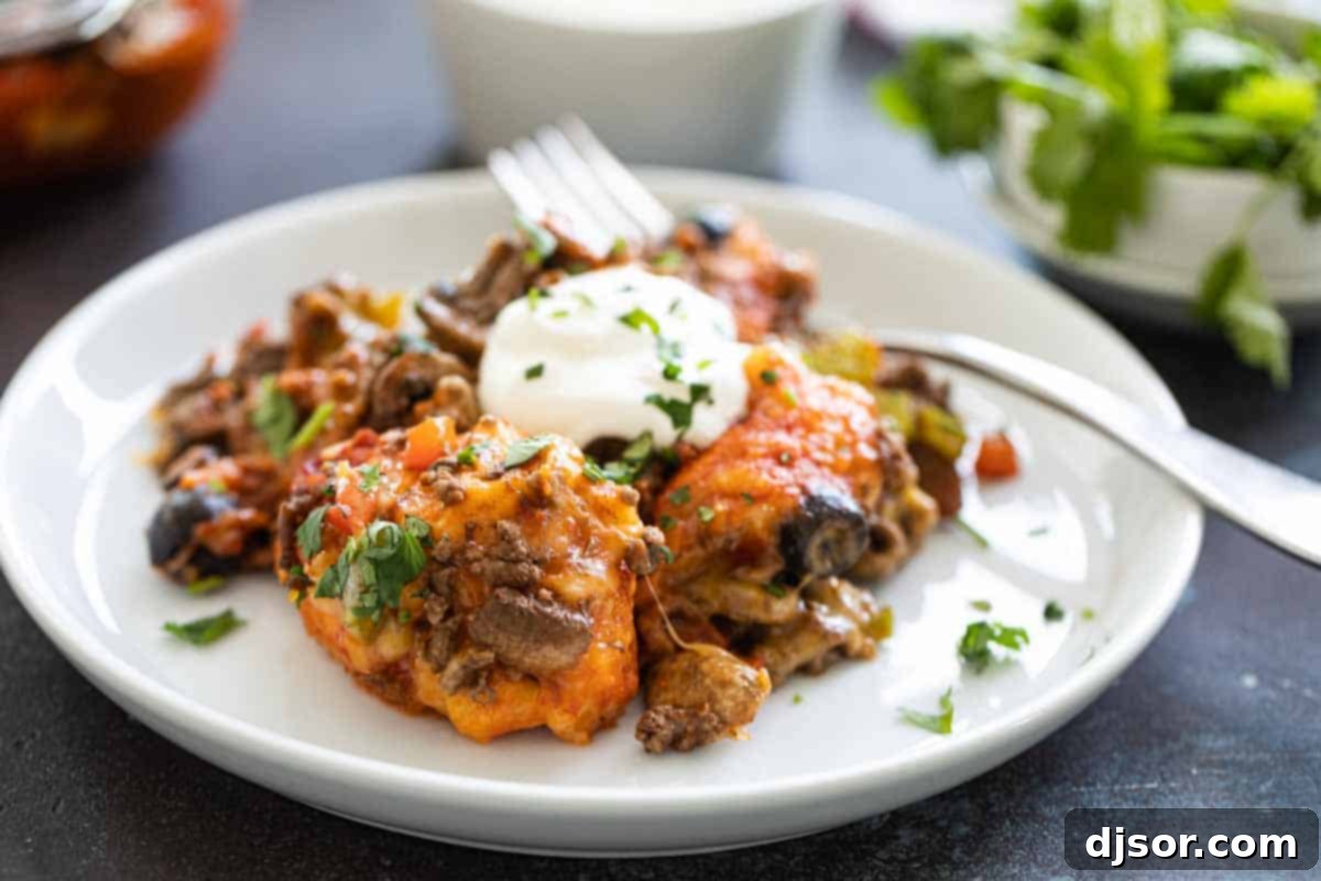 Taco Casserole: Biscuits, taco sauce, spiced ground beef, and cheese come together in this family-friendly dish. Taco casserole served on a white plate with a fork, ready to eat.