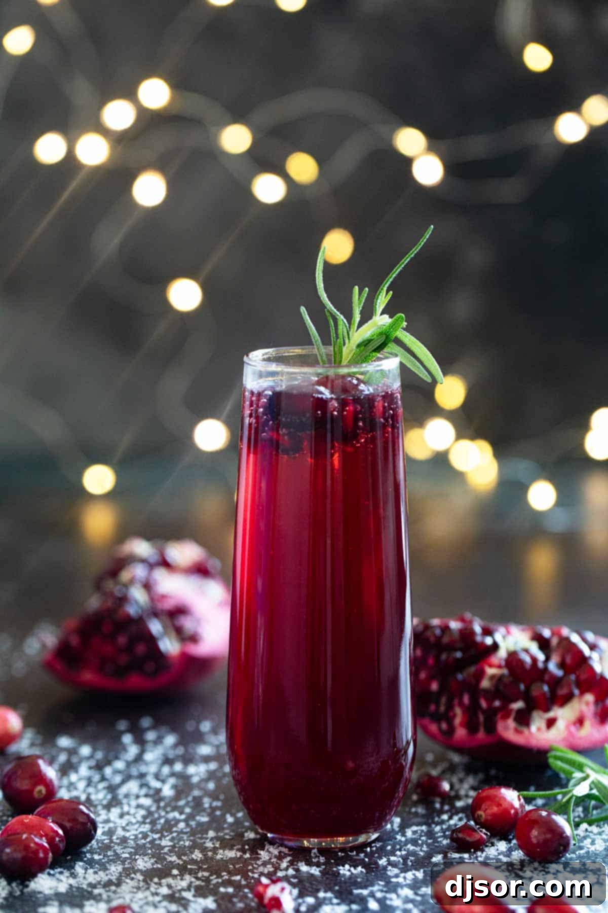 Crimson Pomegranate Cranberry Fizz 6 A single Virgin Pomegranate and Cranberry Bellini in a flute glass, surrounded by fresh pomegranates and cranberries.