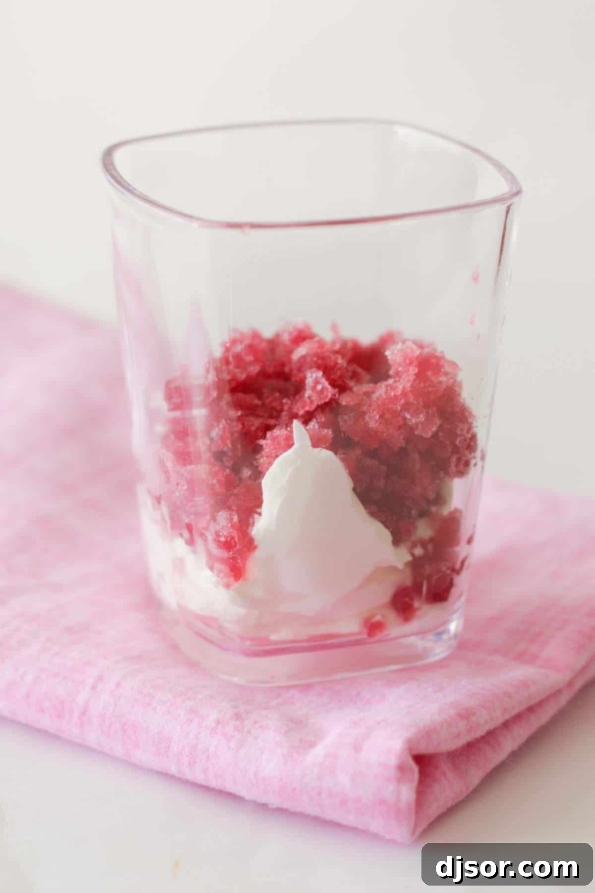 Pomegranate Granita with whipped cream in a clear glass cup, garnished with fresh pomegranate seeds and a mint sprig, ready to be enjoyed.