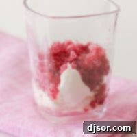 Close-up shot of Pomegranate Granita in a glass with whipped cream, garnished with pomegranate seeds.