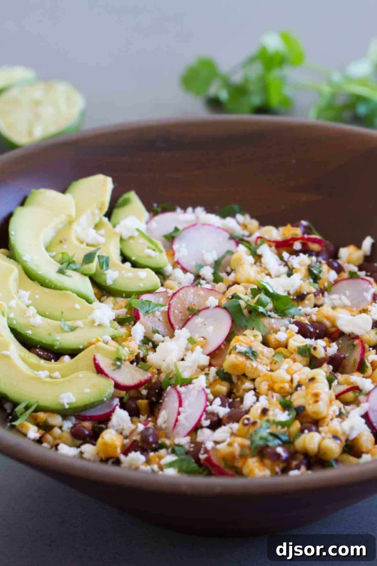 A beautifully arranged salad featuring grilled corn, black beans, creamy avocado slices, and vibrant radishes in a rustic bowl, perfect for a summer meal.