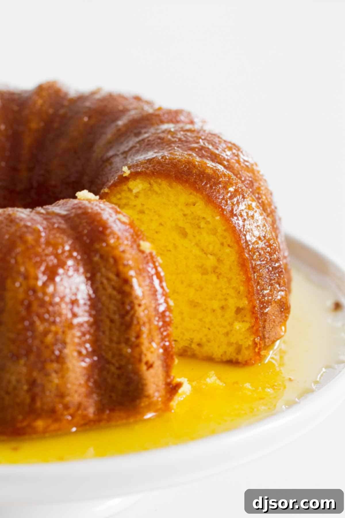 A full view of the golden-brown orange bundt cake, with one slice carefully removed, revealing its moist interior and the thick, shiny glaze.