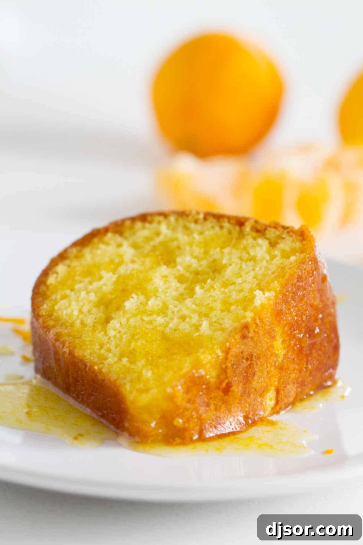 A close-up of a single slice of orange cake on a white plate, glistening with the sweet orange glaze and ready to be enjoyed.
