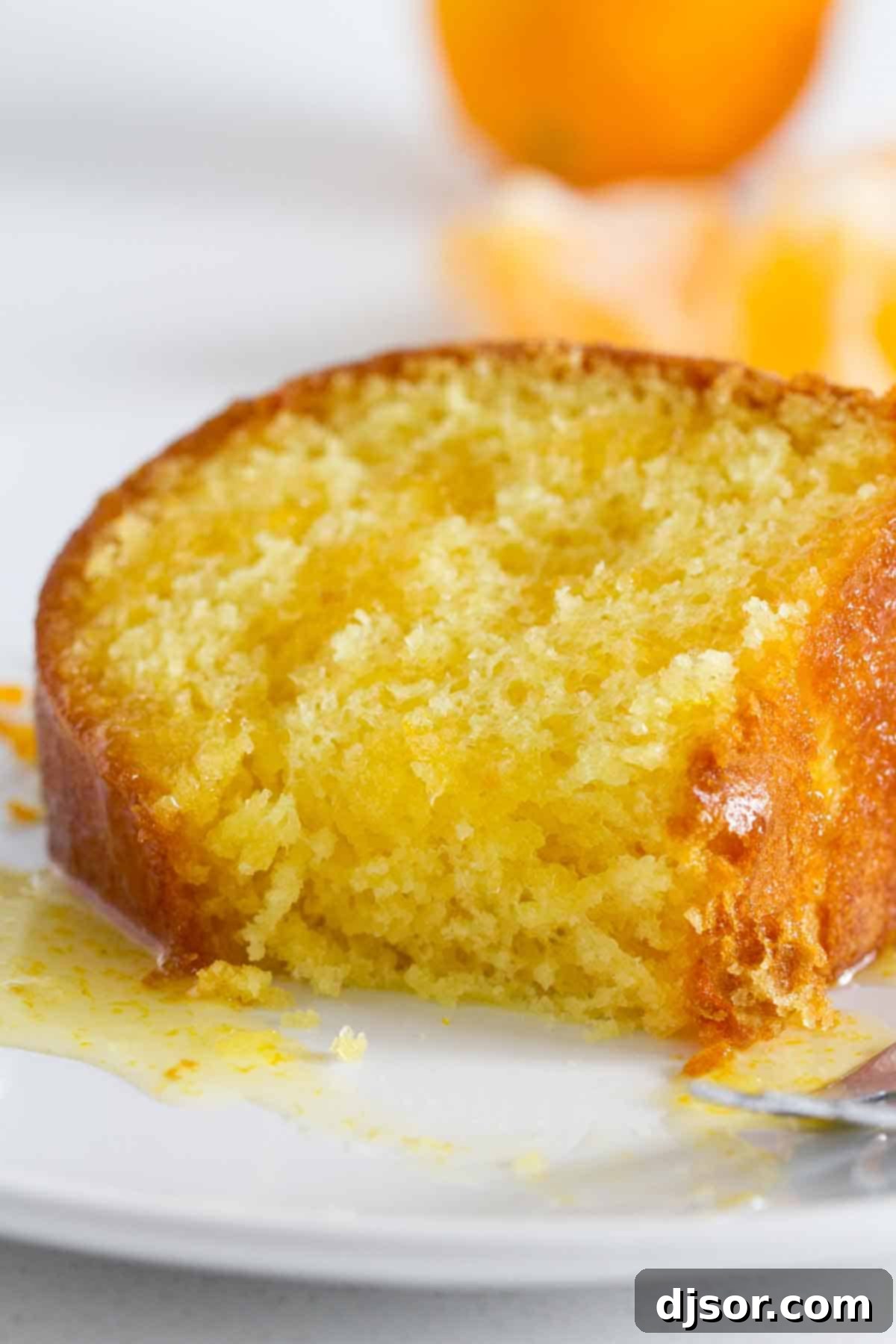 A delectable slice of orange cake on a plate, with a small bite taken, showcasing its moist texture and the appealing orange glaze.