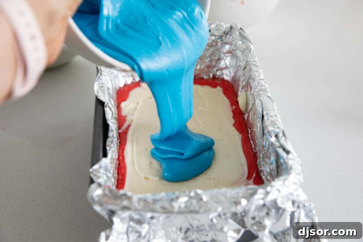 Carefully layering the colorful fudge is essential before creating the signature tie-dye effect for your 4th of July treat. Demonstration of layering the red, white, and blue fudge mixture into the prepared loaf pan for a 4th of July dessert.