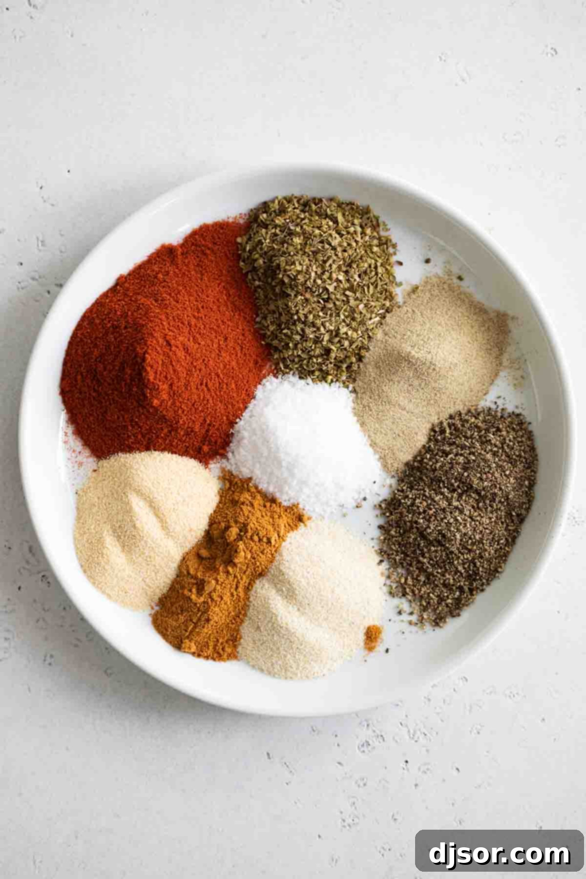 Various individual piles of fresh spices including paprika, oregano, and ground red pepper, laid out before being mixed into a homemade Cajun seasoning blend.