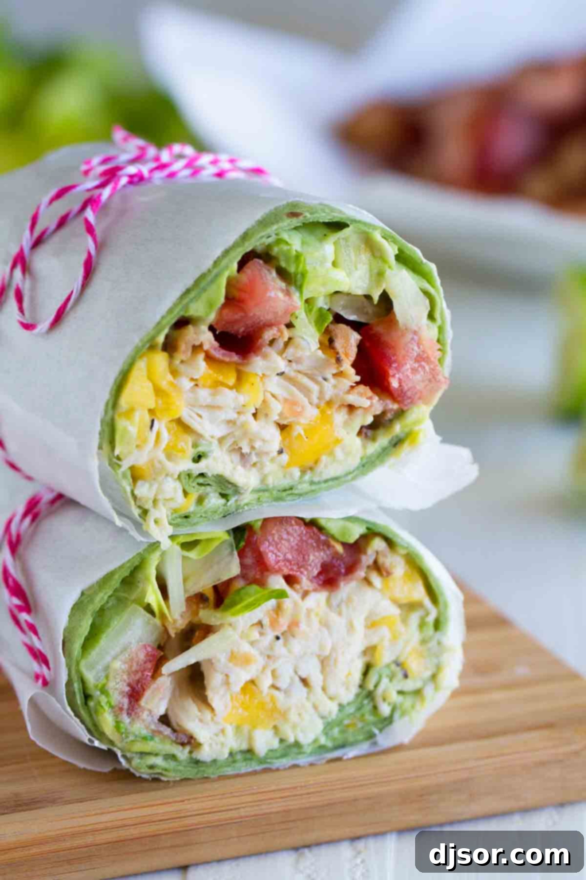 California Club Chicken Wrap cut in half, halves stacked on top of each other, showcasing shredded chicken, mango, avocado, bacon, lettuce, and tomato.