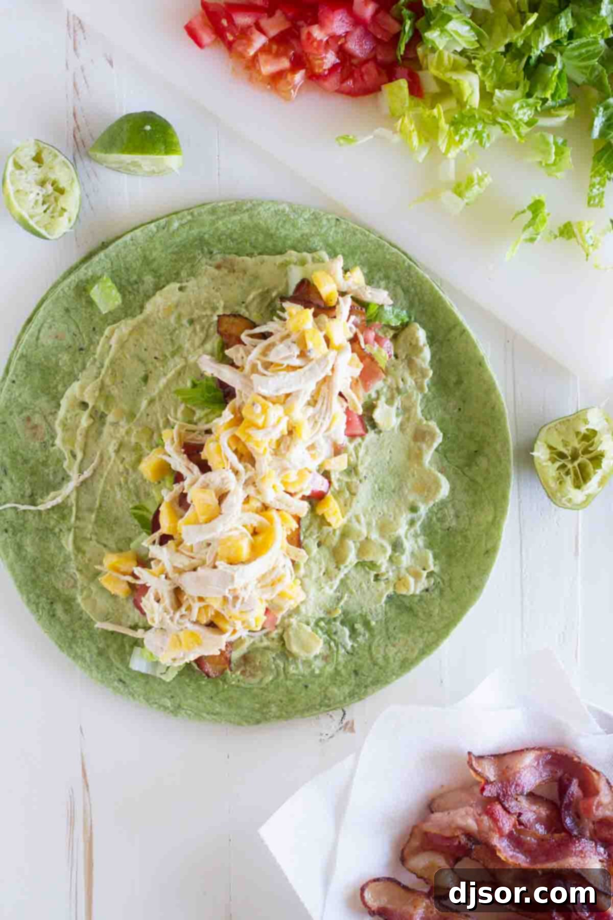 Close-up of a California Club Chicken Wrap showing the colorful fillings inside: shredded chicken, avocado, mango, bacon, lettuce, and tomatoes.
