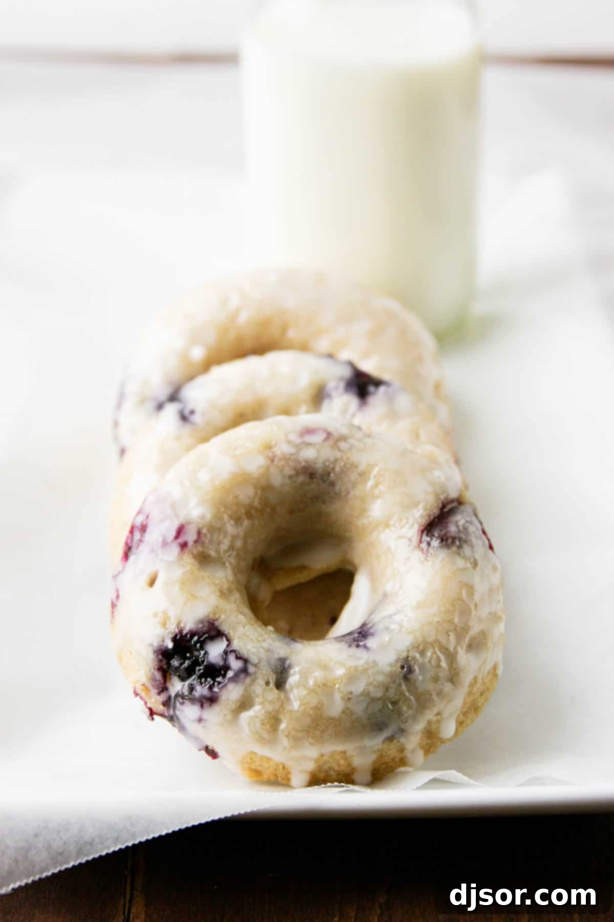 Baked Blueberry Cherry Doughnut Delights 2 Three glazed blueberry cherry baked donuts stacked on a white plate, showcasing their vibrant fruit fillings.