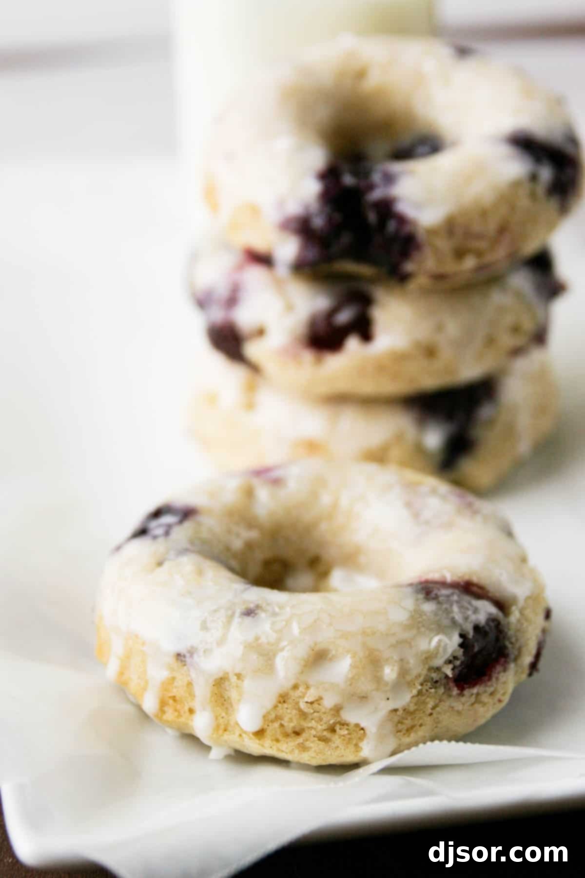 Baked Blueberry Cherry Doughnut Delights 5 A single glazed blueberry cherry baked donut prominently featured, with a stack of three more in the soft background.