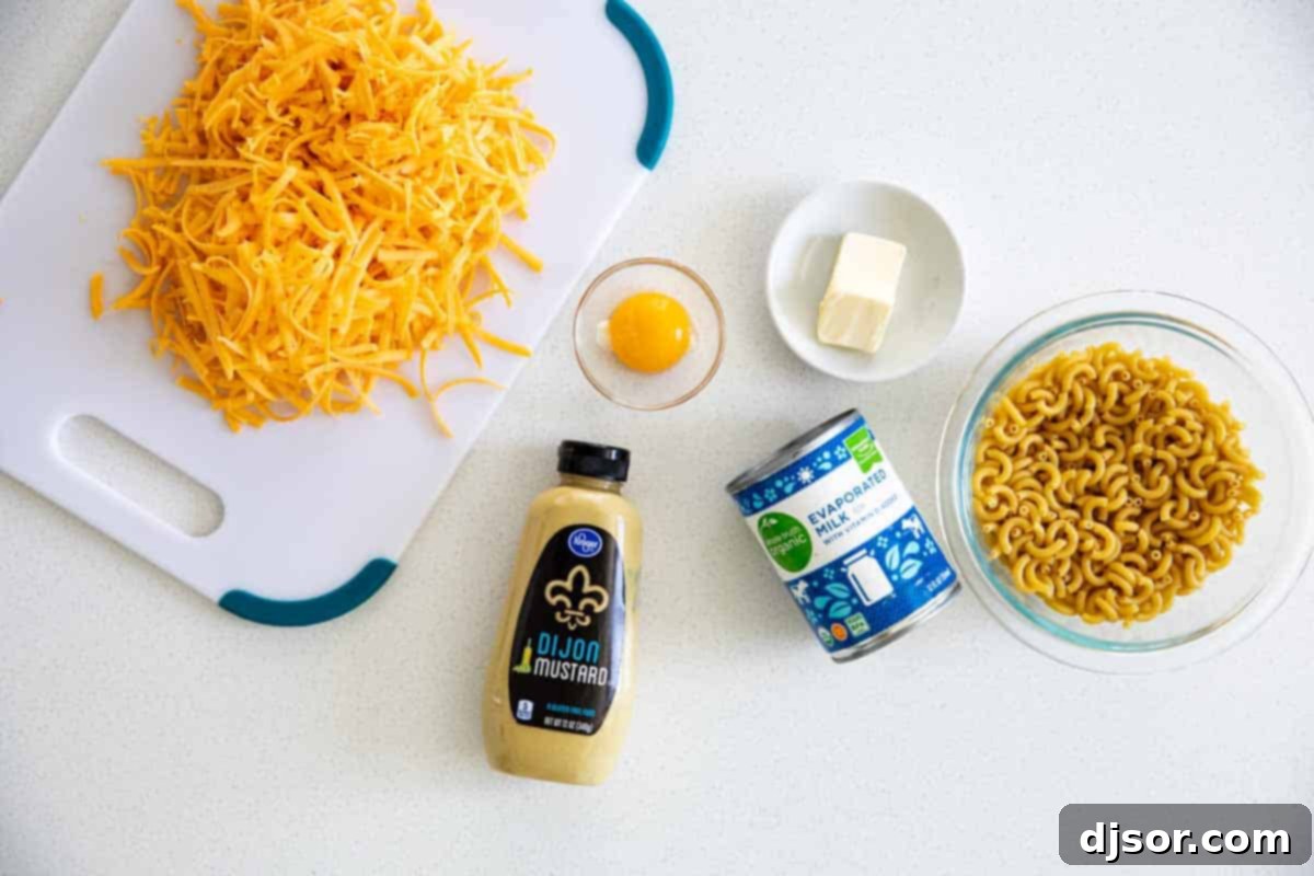 A flat lay showing all the fresh ingredients laid out to make creamy mac and cheese, including macaroni, cheddar cheese, evaporated milk, butter, egg yolk, and Dijon mustard.