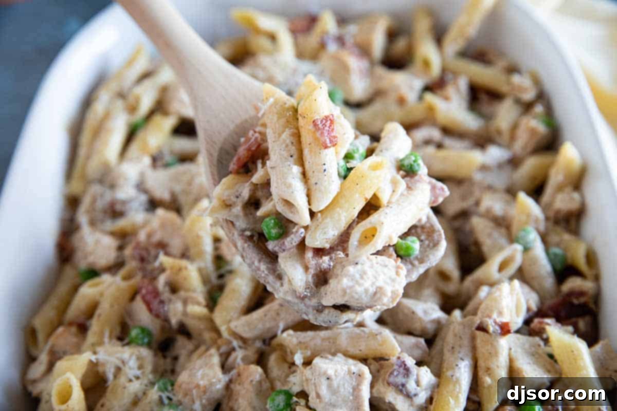 A generous casserole dish filled with creamy Chicken Bacon Pasta, garnished with vibrant green peas. Casserole dish with Chicken Bacon Pasta with peas.