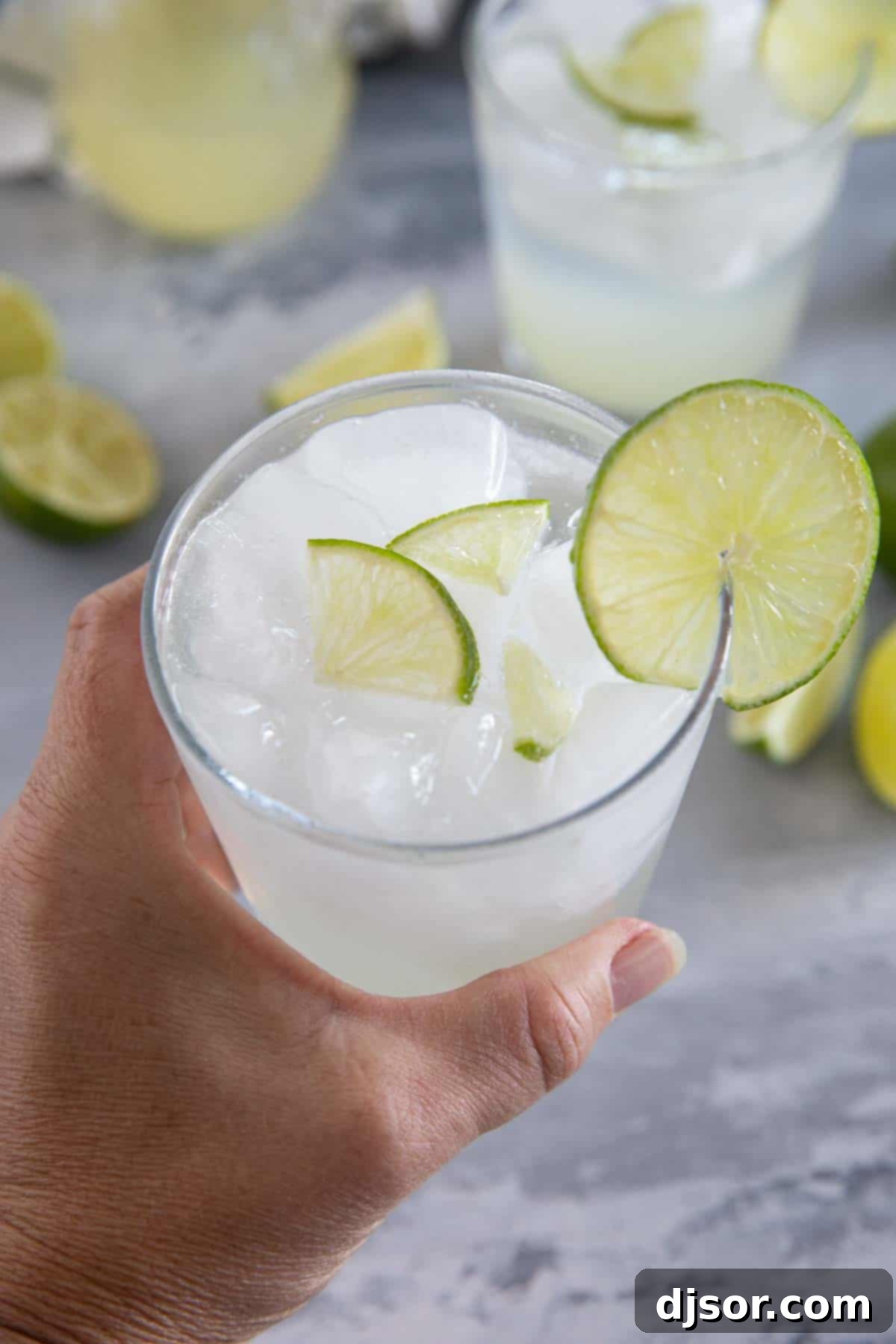 A hand holding a frosty glass of homemade ginger limeade, garnished with fresh lime slices, ready to be enjoyed.