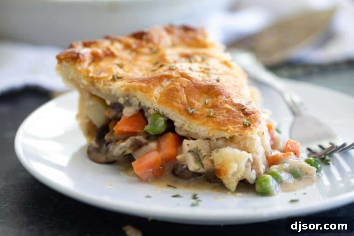 Homemade Chicken Pot Pie: Tender Chicken, Creamy Gravy, Flaky Crust A perfectly golden slice of homemade chicken pot pie on a white plate, showcasing its flaky crust and rich, creamy filling brimming with chicken and vegetables.