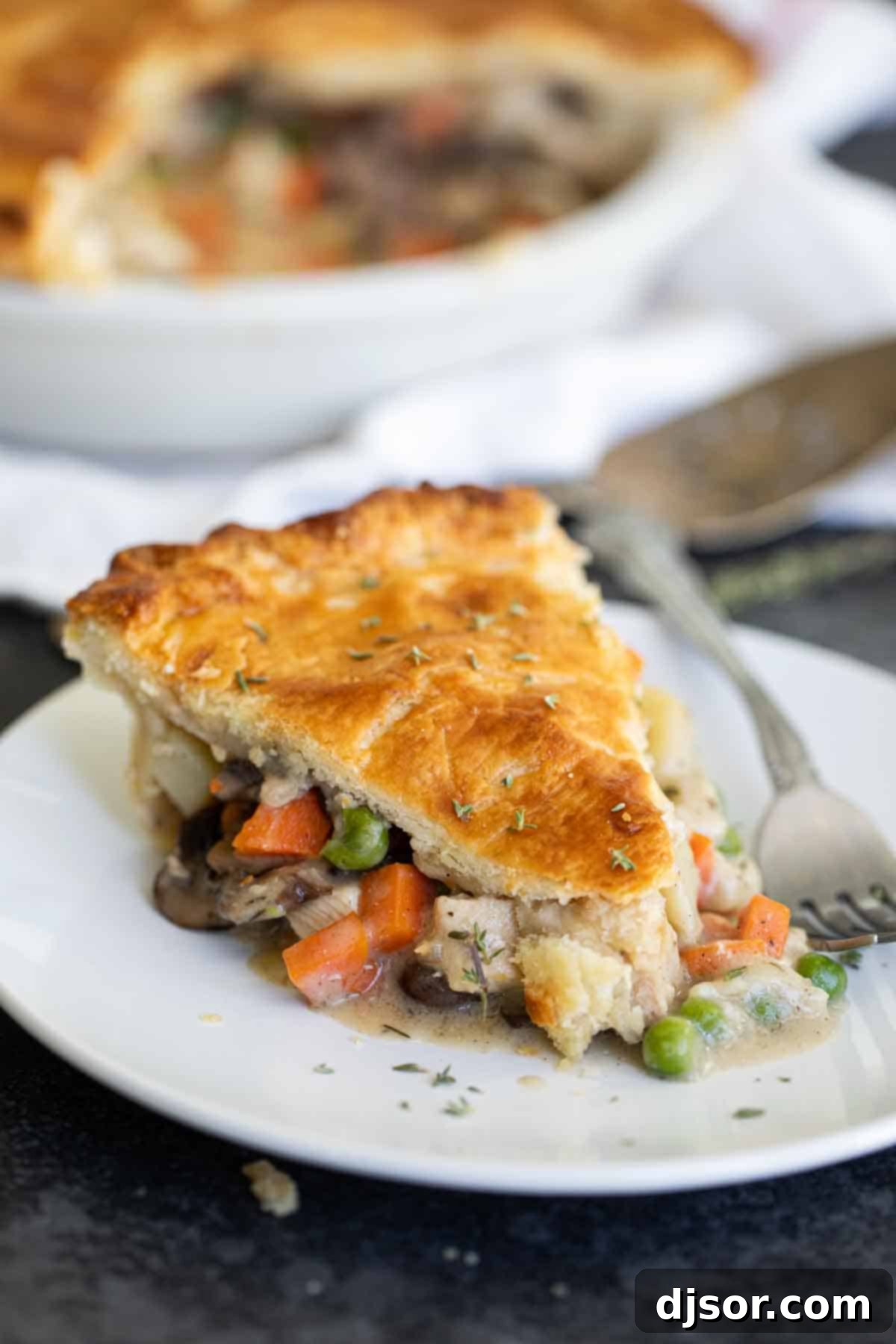Ultimate Comfort Chicken Bake 2 A slice of homemade chicken pot pie on a plate, with the full pie in a baking dish blurred in the background, ready to be enjoyed.