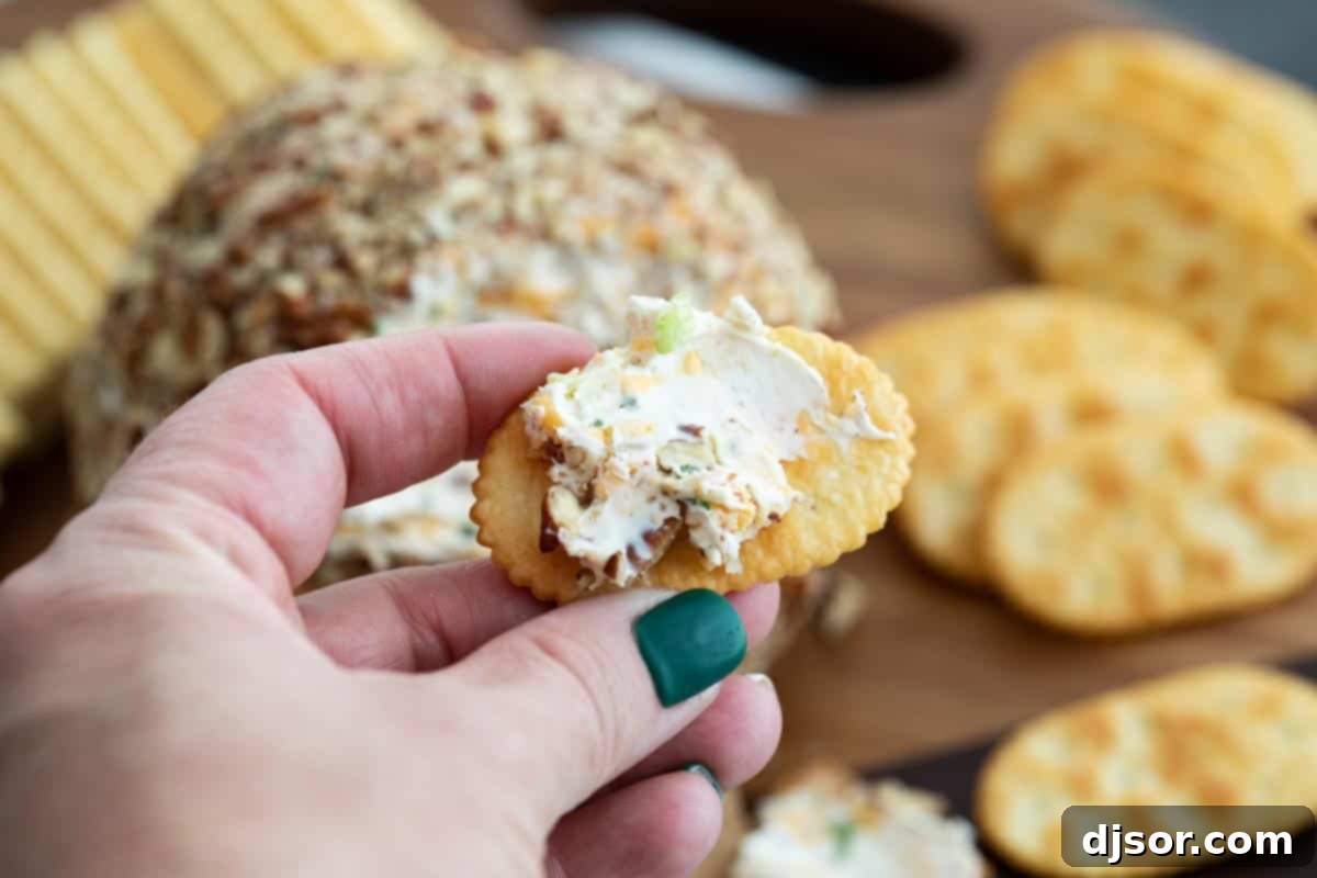 A classic appetizer that is perfect for a party, this Cheese Ball Recipe is the only one you’ll need! Filled with cheese and spices and coated in pecans, it is always a crowd favorite. A generous serving of creamy cheese ball, rich with herbs and spices, spread elegantly onto a crisp, golden cracker, showcasing the delightful texture and inviting appeal of this classic appetizer. The cheese ball is ready to be enjoyed.