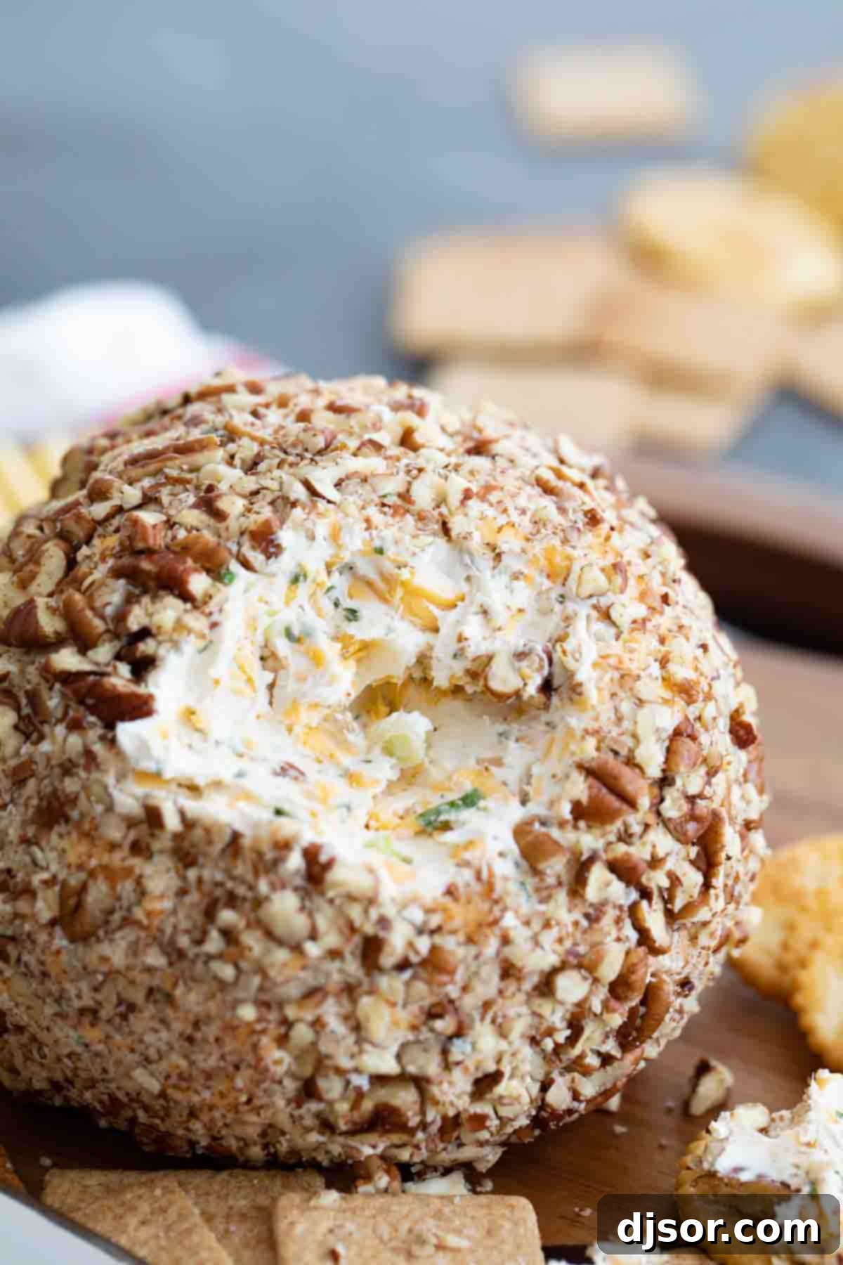 A classic appetizer that is perfect for a party, this Cheese Ball Recipe is the only one you’ll need! Filled with cheese and spices and coated in pecans, it is always a crowd favorite. A visually inviting close-up of a large, perfectly sliced cheese ball, revealing its smooth, creamy interior studded with herbs and spices, and a dense, crunchy pecan coating, presented on a white plate ready for serving, highlighting its irresistible texture.