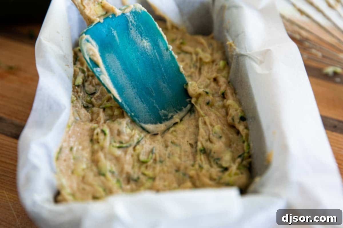 The best classic Zucchini Bread Recipe! A great way to use up that surplus of zucchini, this quick bread recipe is easy and perfectly spiced. Zucchini bread batter being spread into a parchment paper-lined loaf pan before baking.