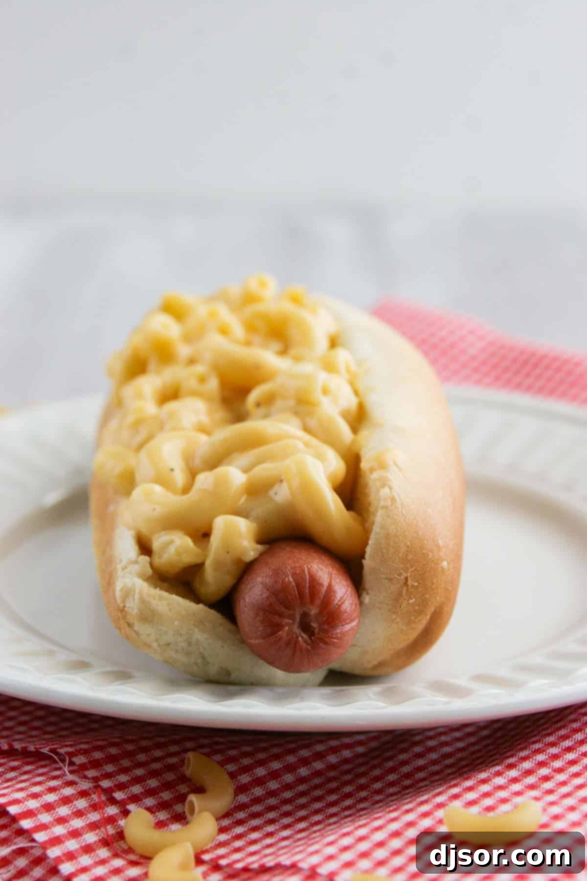 A perfectly cooked hot dog nestled in a bun, generously topped with creamy, golden homemade Mac and Cheese.