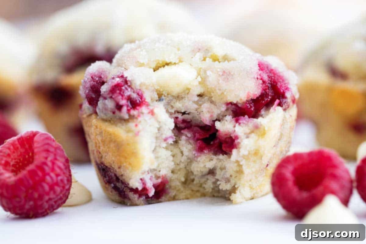 Sweet raspberries and creamy white chocolate make these Raspberry Muffins with White Chocolate Chips a special breakfast treat! They are soft and moist and perfectly sweet. raspberry muffin with a bite taken to show the inside texture