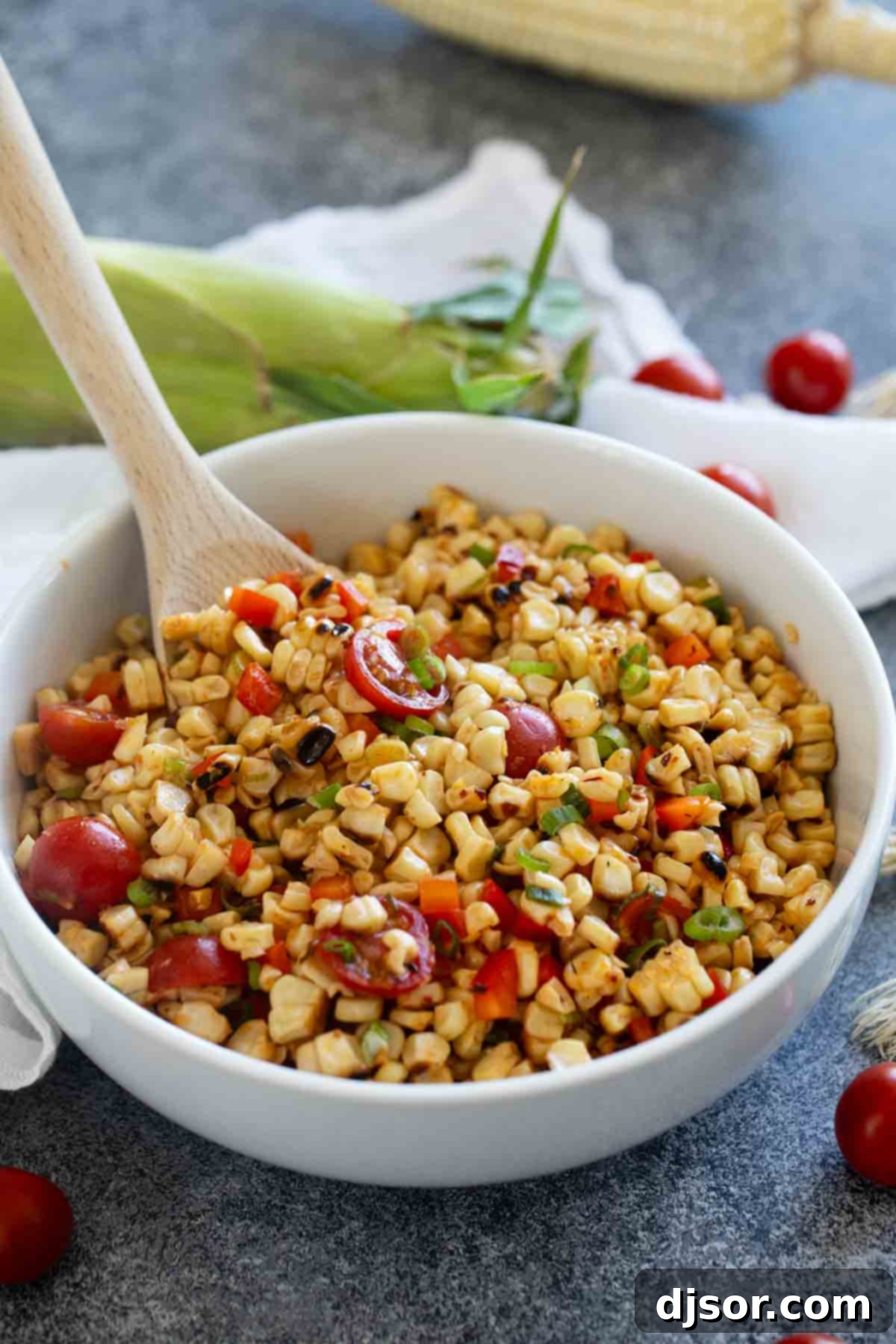 A vibrant bowl of grilled corn salad featuring charred corn kernels, bright red tomatoes, crisp bell pepper, and fresh green onions in a white serving bowl.