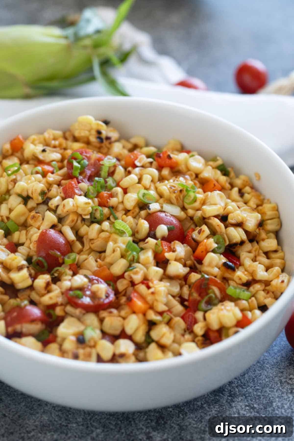 A close-up of a large white bowl filled with vibrant grilled corn salad, showcasing the golden corn, red tomatoes, and green onions.