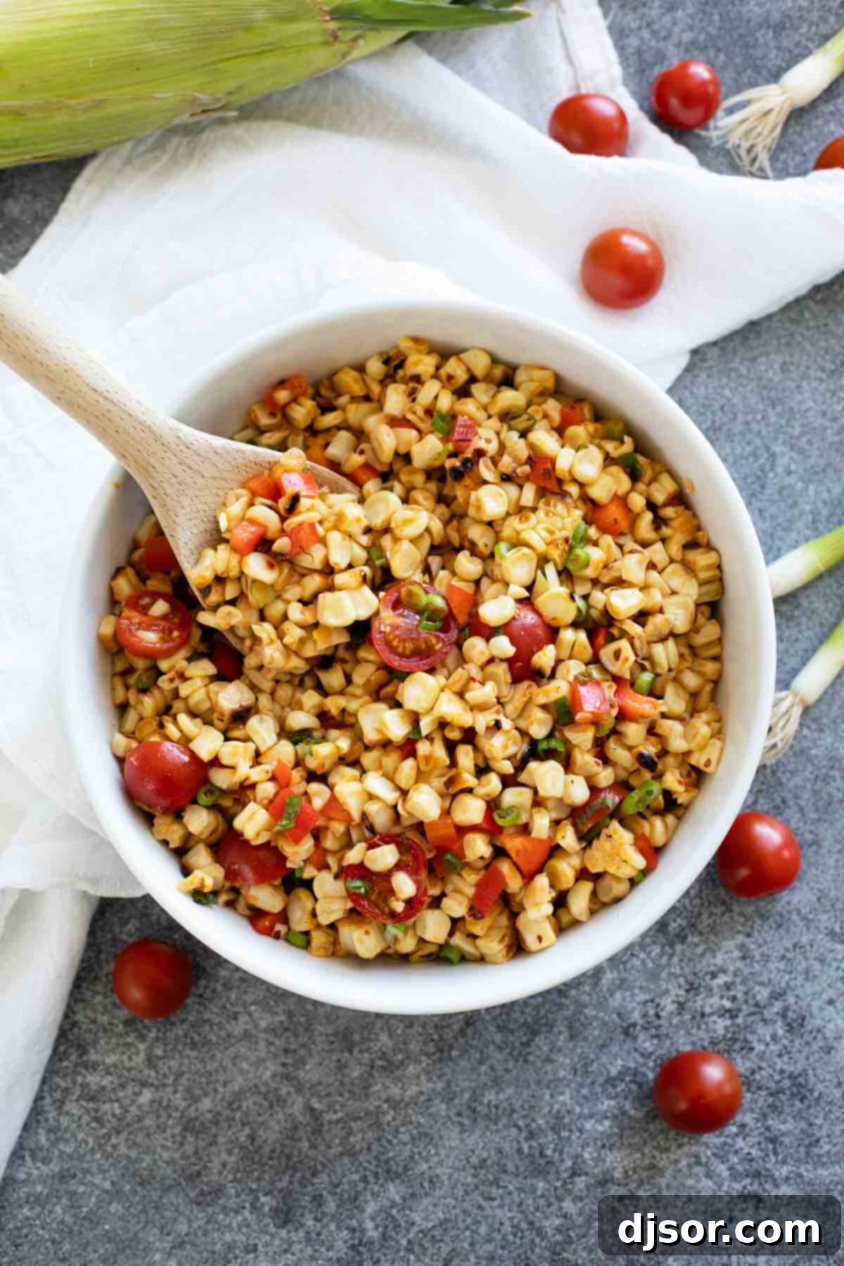 A large white bowl brimming with grilled corn salad, featuring a wooden spoon resting inside, ready for serving.