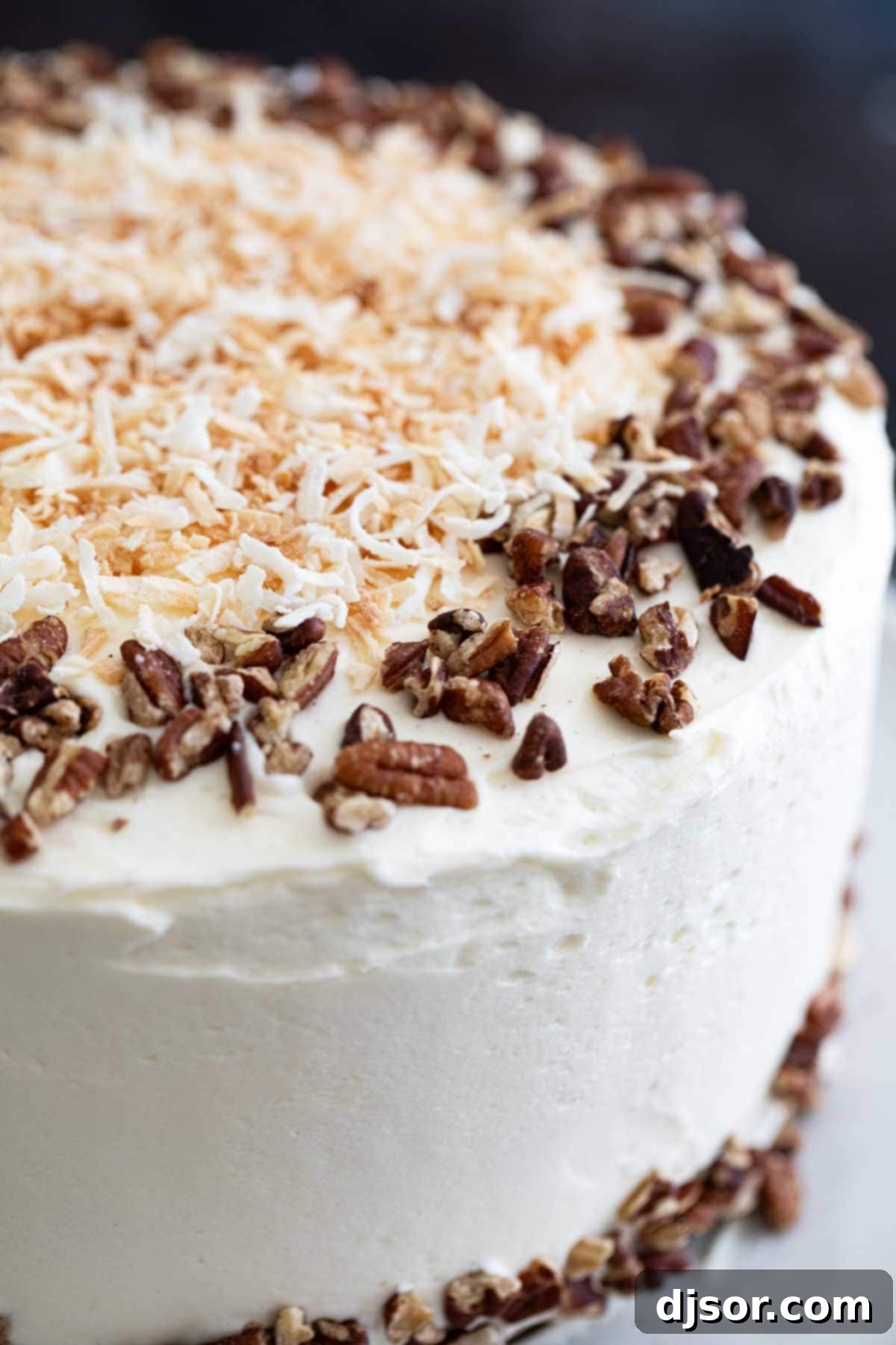 A stunning three-layer carrot cake generously topped with cream cheese frosting, garnished with toasted coconut flakes and chopped pecans, presented on a rustic cake stand.