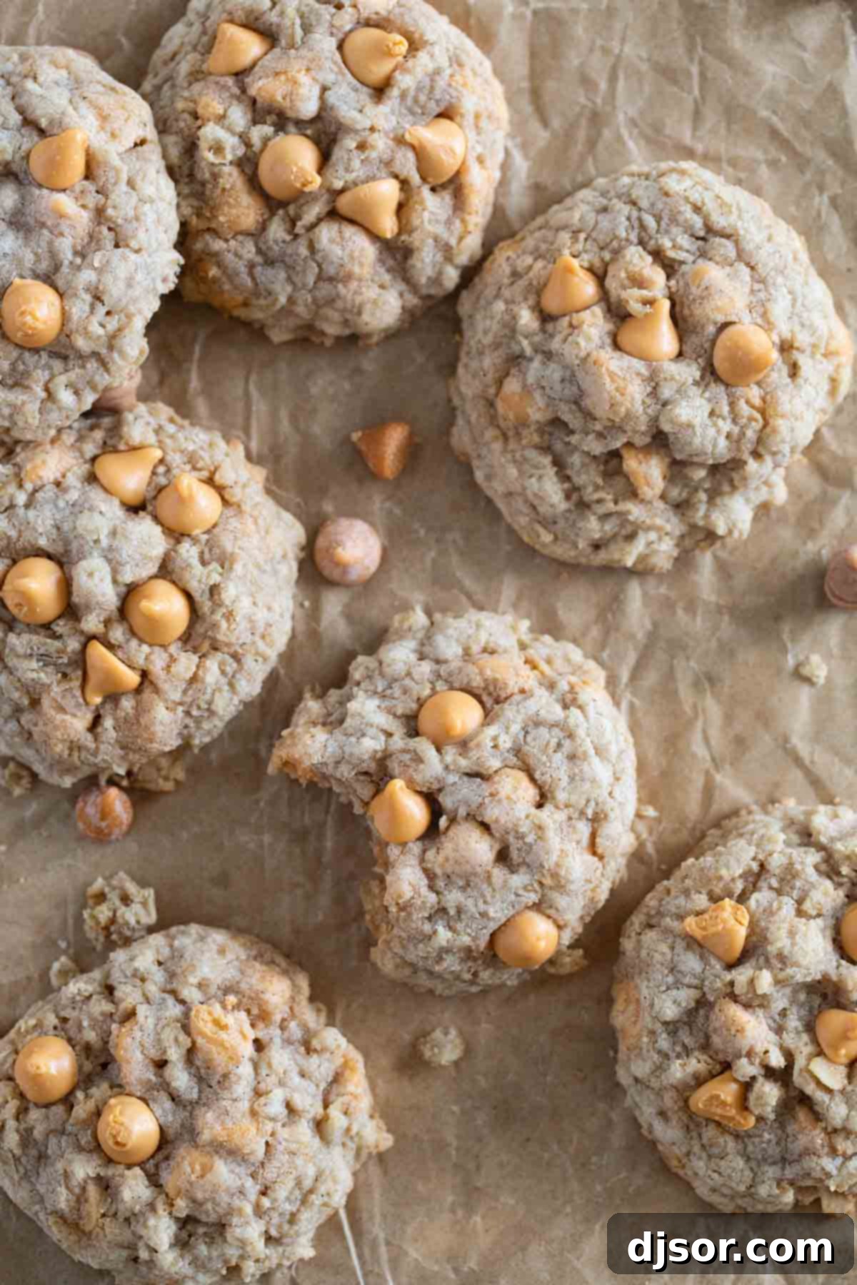 A close-up of Oatmeal Scotchies cooling on parchment paper, with one cookie showing a bite taken out, revealing its soft, chewy interior filled with oats and butterscotch.