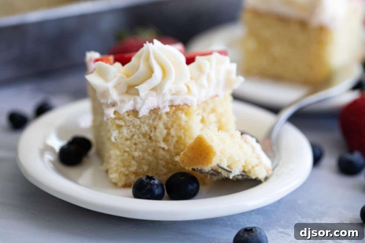 A fork taking a bite out of a slice of flag cake, showing the soft cake and creamy frosting with fruit.