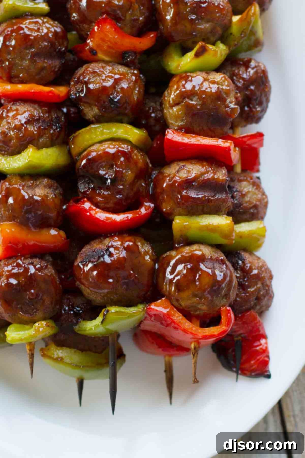 Glistening sweet and sour meatballs and peppers on skewers Close-up of grilled skewers featuring meatballs and bell peppers coated in a glistening sweet and sour sauce.