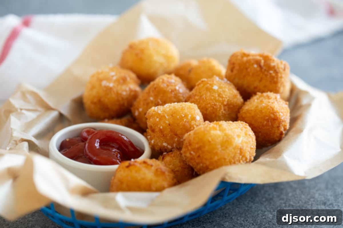A rustic basket overflowing with golden-brown homemade tater tots, with a small ramekin of bright red ketchup beside it.