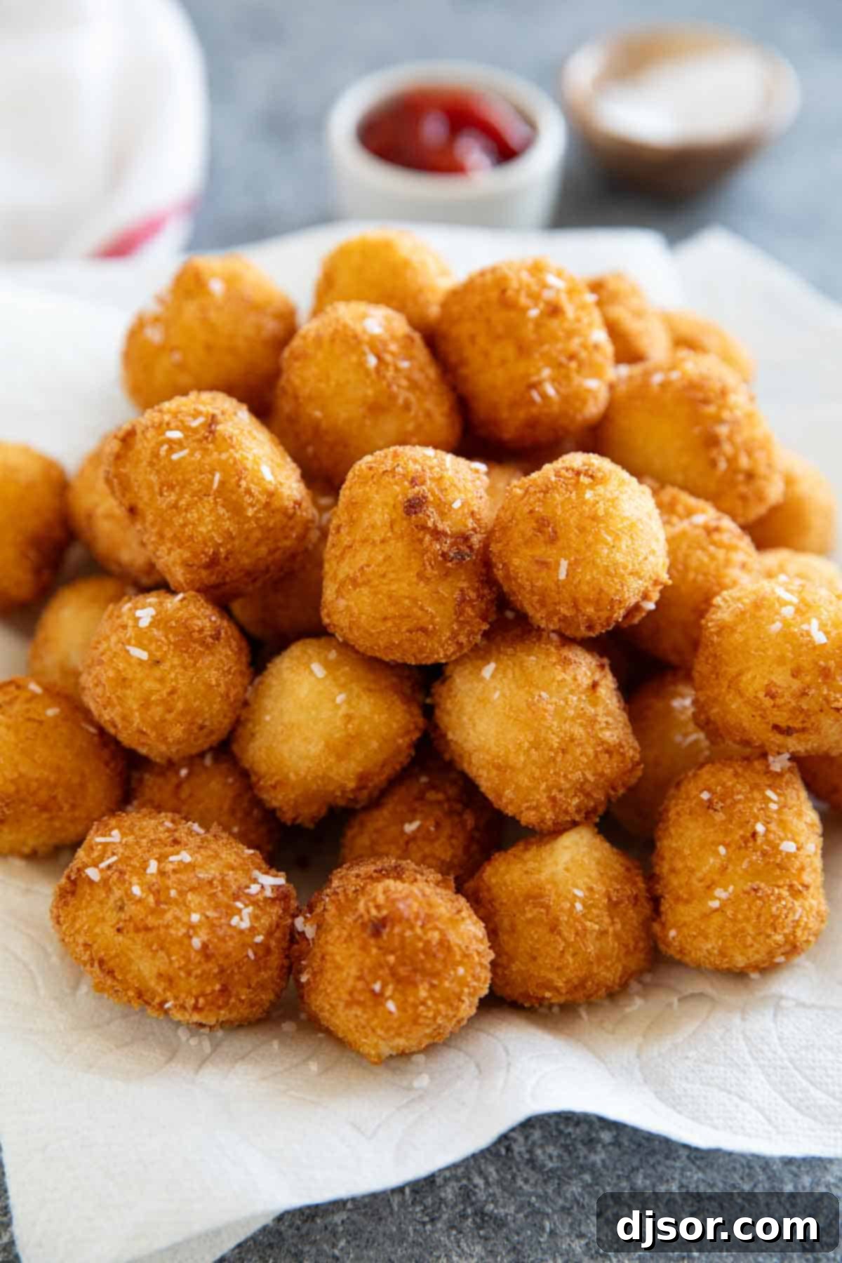 A plate lined with paper towels, holding a fresh batch of steaming, golden-brown homemade tater tots, ready to be seasoned.