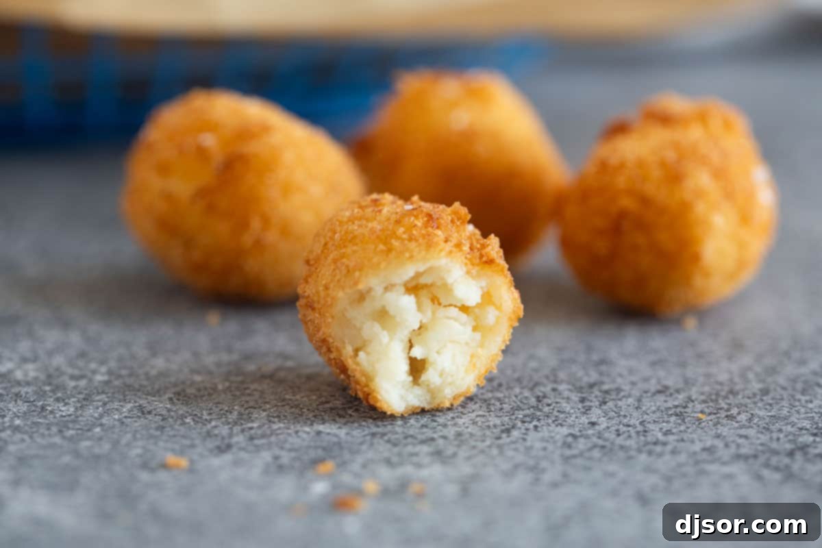 A close-up of homemade tater tots, with one tot cut in half to reveal its soft, creamy mashed potato interior and crispy golden crust.