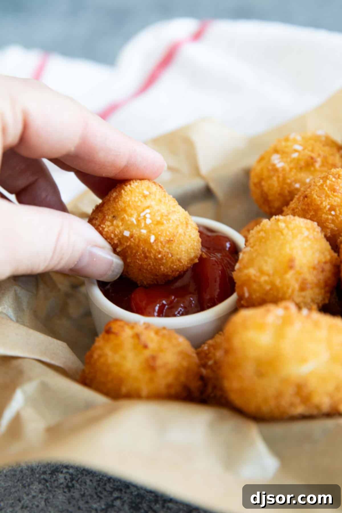 A hand dipping a crispy homemade tater tot into a small bowl of ketchup, highlighting its golden texture.