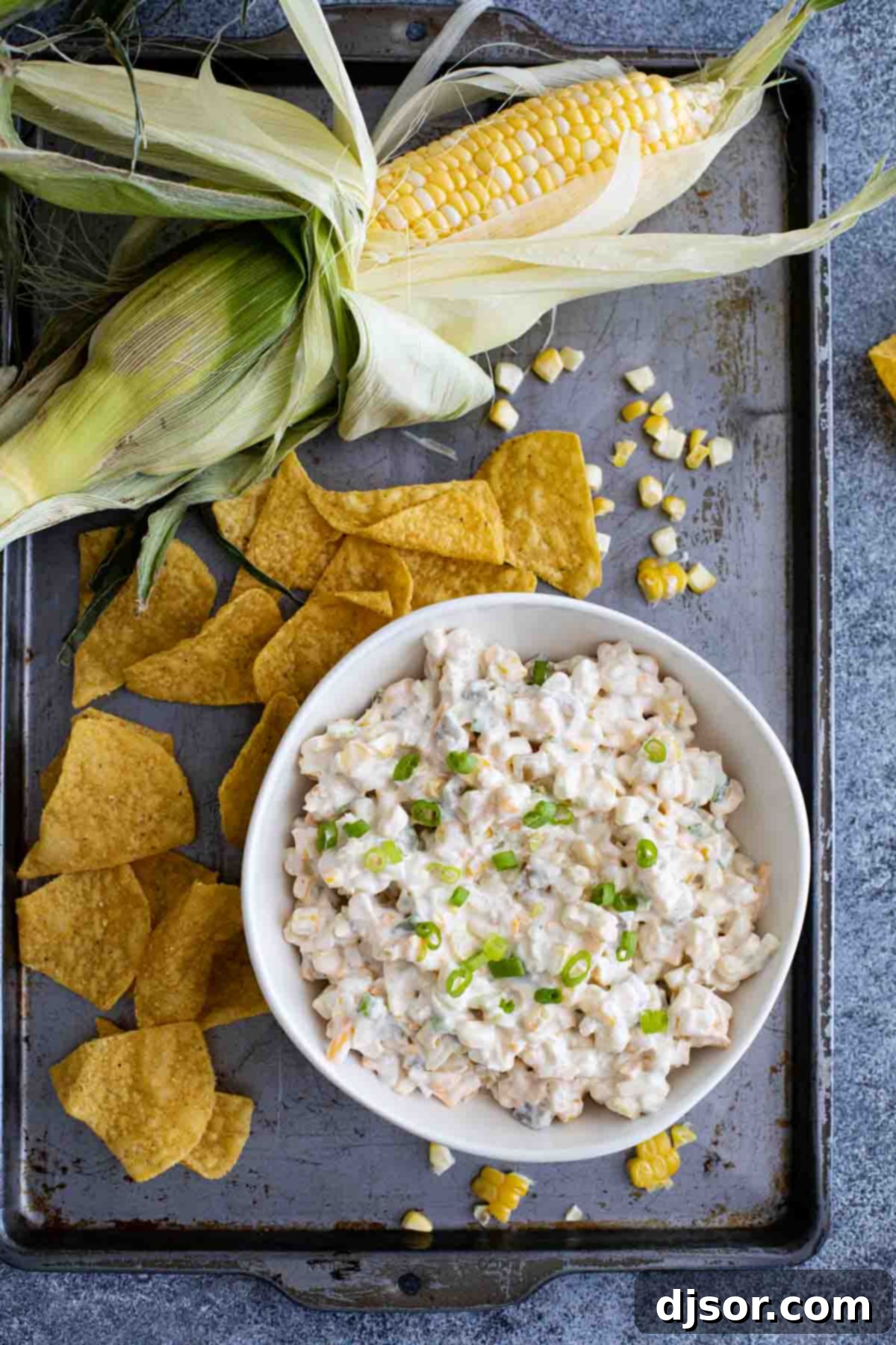 Easy party corn dip served on a baking sheet with tortilla chips and fresh corn cobs.
