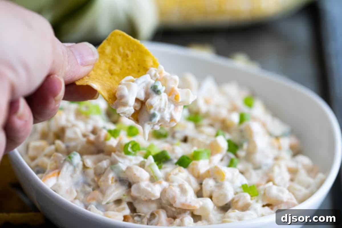 A chip being dipped into creamy Green Chile Corn Dip.