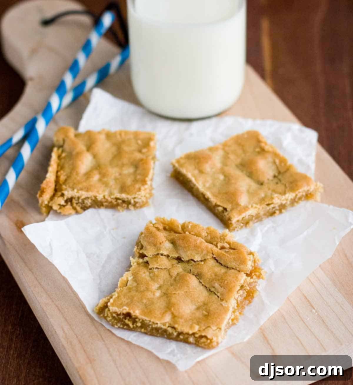 Sweet and buttery with a hint of coconut, these butterscotch bars are super easy and crowd pleasing. Sliced Butterscotch Bars arranged on a rustic cutting board, accompanied by glasses of milk and straws, highlighting their golden-brown color and chewy texture.